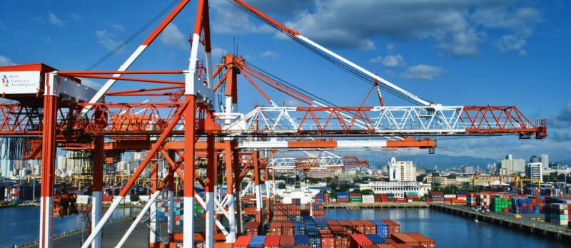 Containerhafen mit großen Verladekränen und gestapelten bunten Containern am Wasser, Logistik und Schifffahrt im Hintergrund.