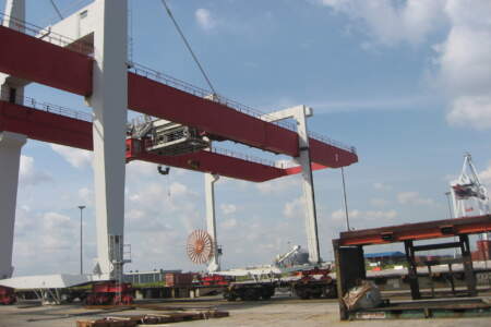 Große rote und weiße Portalkräne auf einem Containerterminal im Hafen bei blauem Himmel, Umschlagplatz für Container und Güter.