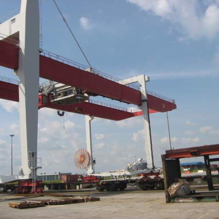 Große rote und weiße Portalkräne auf einem Containerterminal im Hafen bei blauem Himmel, Umschlagplatz für Container und Güter.
